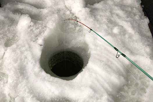 snow surrounded circular hole in the ice with a short fishing rod with its line caste inside it