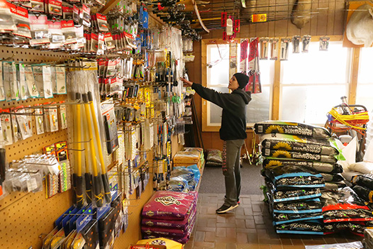 Woman standing in front of fishing gear beside large bags of wild bird feed and other outdoor supplies