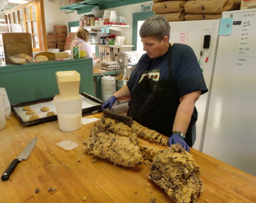 woman cutting up large amount of chocolate chunk cookie dough with a pastry knife